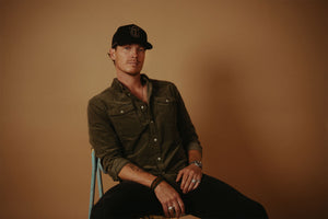 Man wearing a cap and button-up shirt sitting against a brown background george Birge